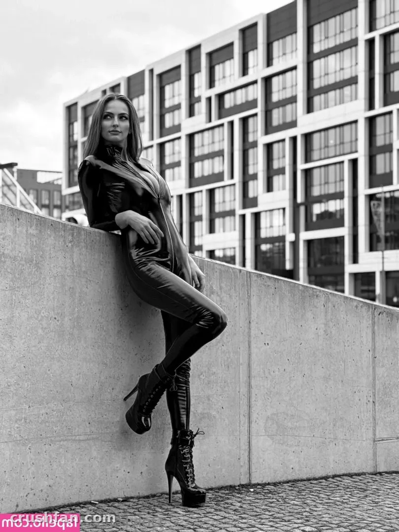 Black-and-white photo of LUSILOVE in a leather jacket and trousers leaning against a concrete wall