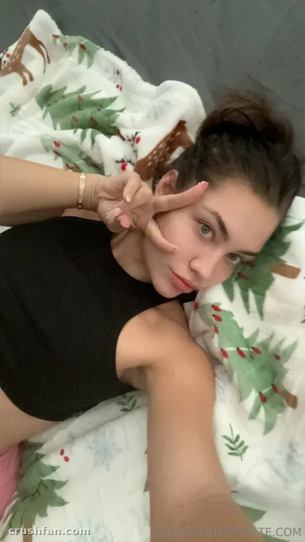Cel in a black top lying on a patterned blanket and making a peace sign