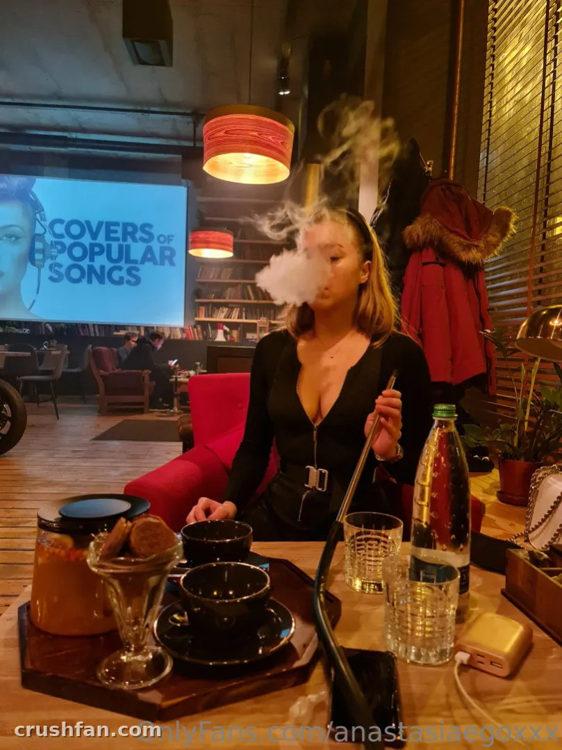 Femme en haut noir exhalant de la fumée à une table dans un salon chaleureux.