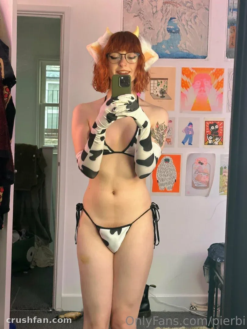 Pierbi de biquíni estampado de vaca tirando uma selfie no espelho em uma sala com arte de parede colorida.