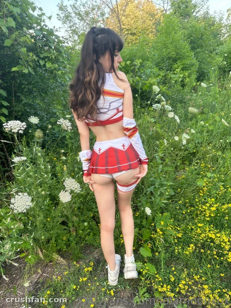 Creator in a red and white cosplay outfit standing among wildflowers and greenery outdoors