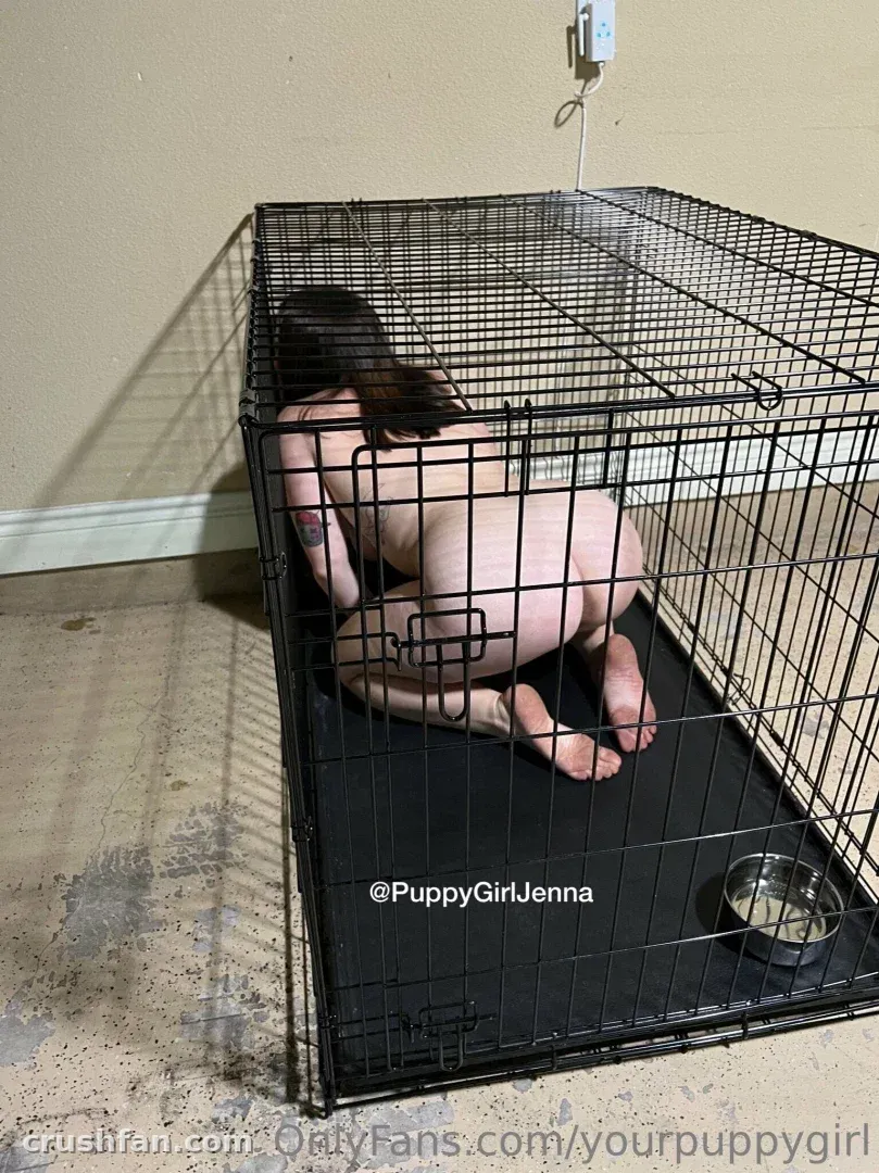 Jenna kneeling inside a black wire crate on a dark mat in a plain room