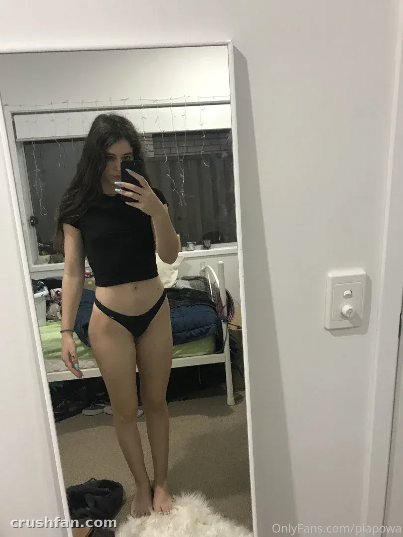 PiaPowa en crop top noir et bas de bikini prenant un selfie dans le miroir dans une chambre