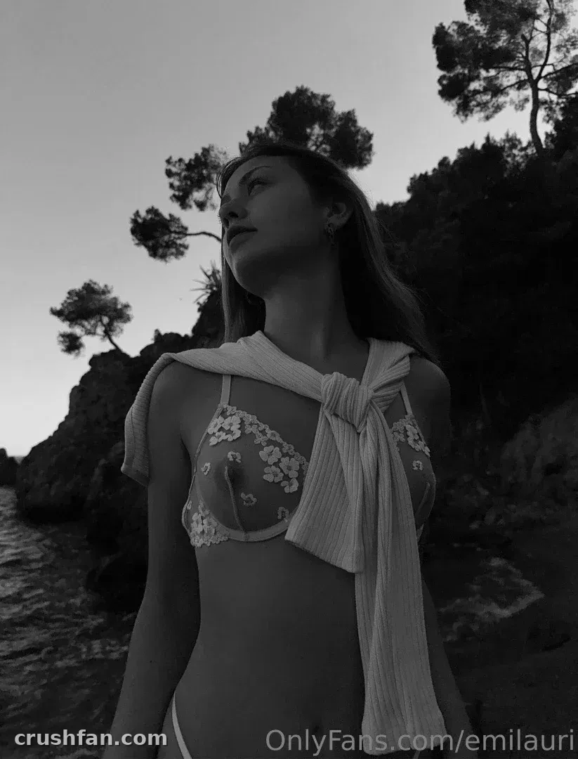 Emilauri in black and white standing by a rocky coast with draped fabric over her shoulders.