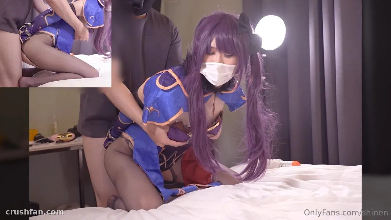Haru em uma fantasia azul e dourada com cabelo roxo sobre roupa de cama branca em um quarto iluminado.