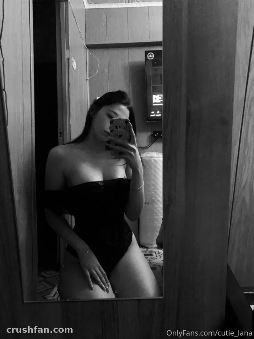 Cutie Lana en body noir prenant un selfie miroir en noir et blanc à l'intérieur