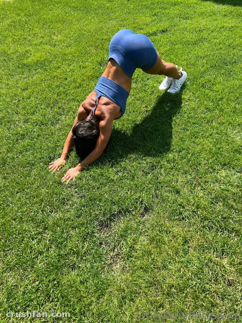 Miss Lexa in blue activewear stretching on a green lawn in bright sunlight.