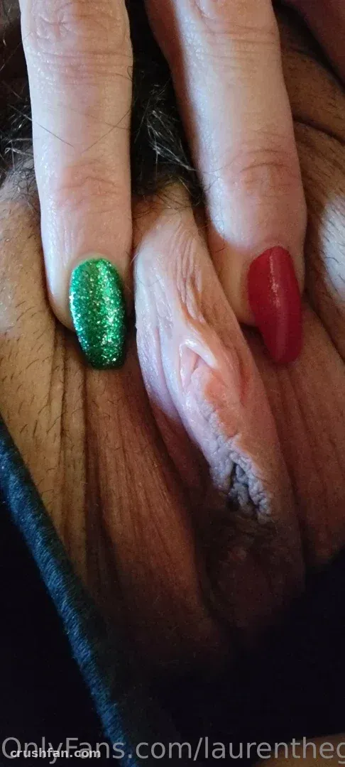 Close-up of two fingernails, one glittering green and one glossy red, against a dark textured surface.