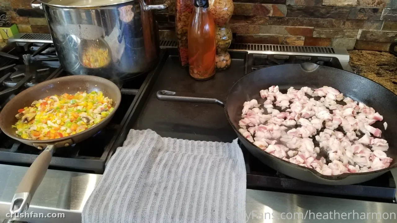 Two pans of food and a large pot on a stovetop with a folded grey cloth in front
