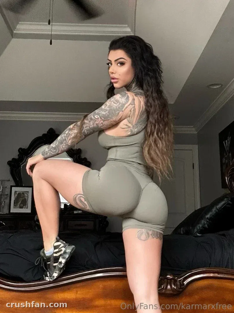 Karma Rx con un conjunto de dos piezas color salvia de pie sobre una cama en un dormitorio con iluminación suave