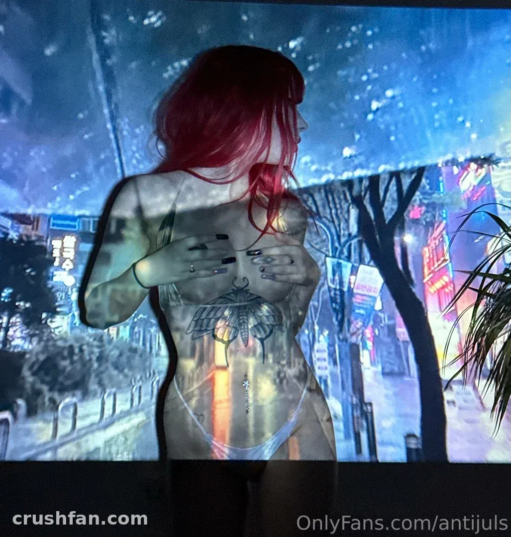 Juls aux cheveux roux et tatouages posant devant une projection urbaine au néon