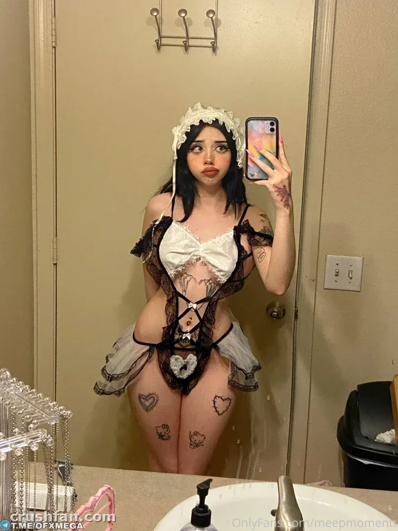 Mirror selfie of a woman in a black and white lace maid costume in front of a beige door