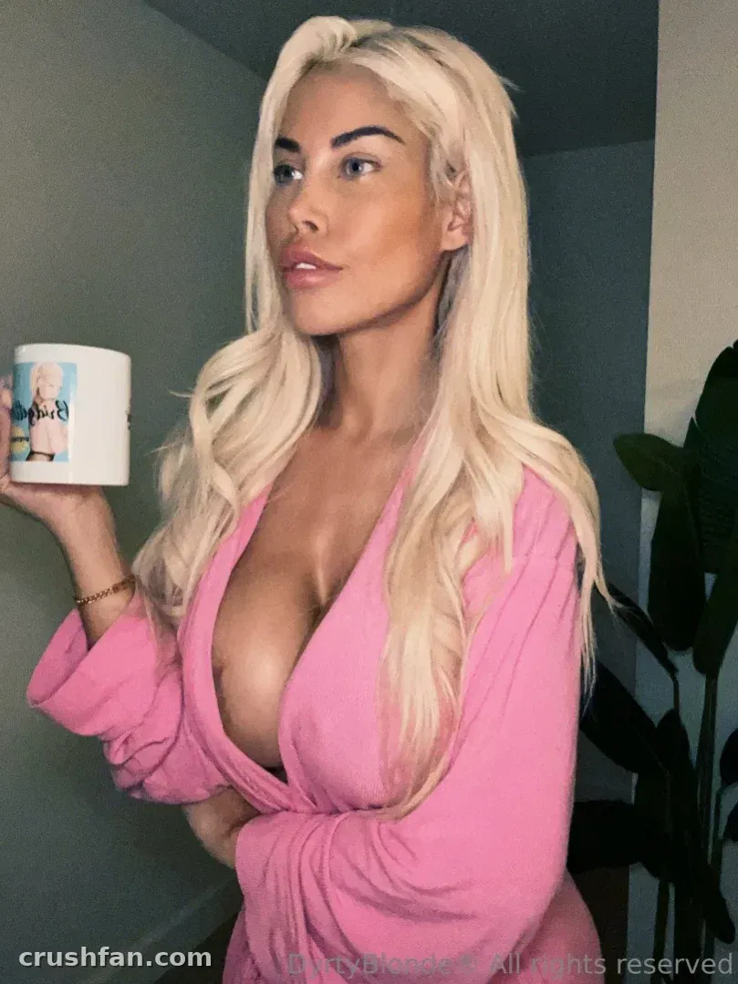 Bridgette B de roupão rosa segurando uma caneca branca em ambiente interno
