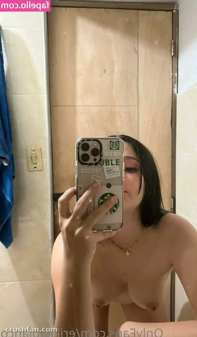 Erikka Blanco segurando um celular para uma selfie no espelho em um banheiro de azulejos