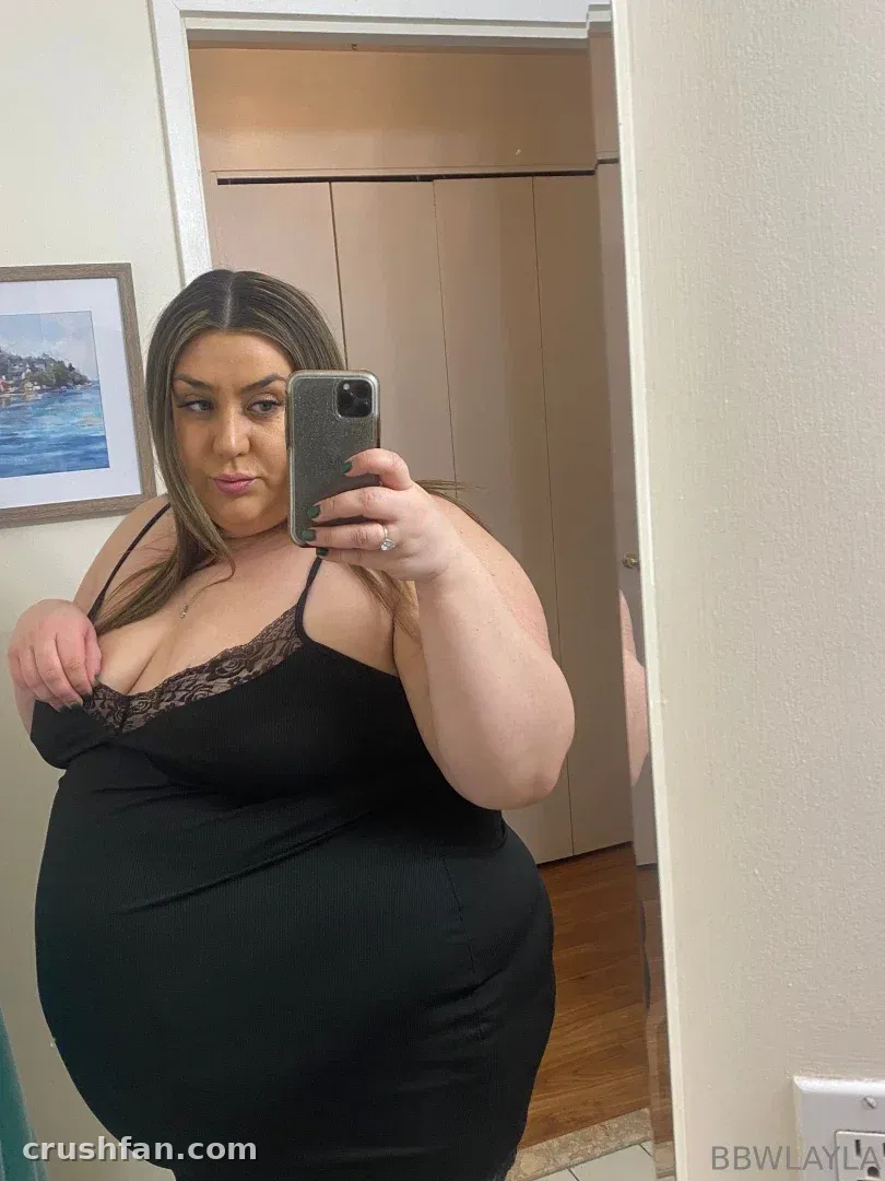 BBW Layla in a black lace-trimmed dress taking a mirror selfie indoors
