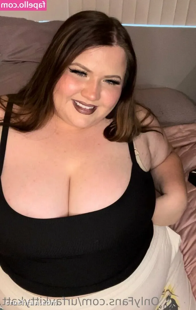 Mulher sorridente com um top preto sentada em uma cama contra uma cabeceira macia