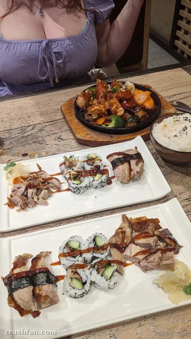 Pratos de sushi e uma tigela de arroz sobre uma mesa de madeira com uma mulher de blusa lavanda.