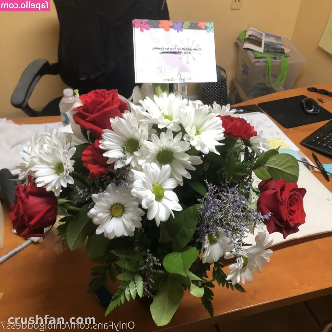 Bouquet of red roses and white daisies on a wooden desk beside a keyboard and office chair