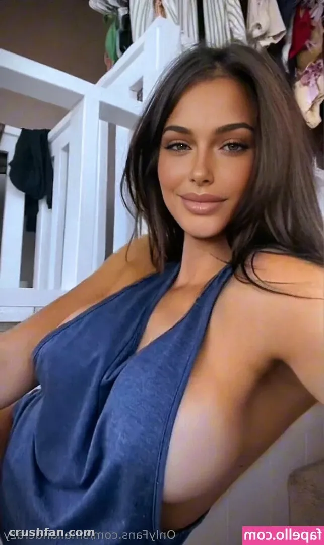 Hailey Miller com um top halter azul posando em ambiente interno ao lado de uma estrutura branca