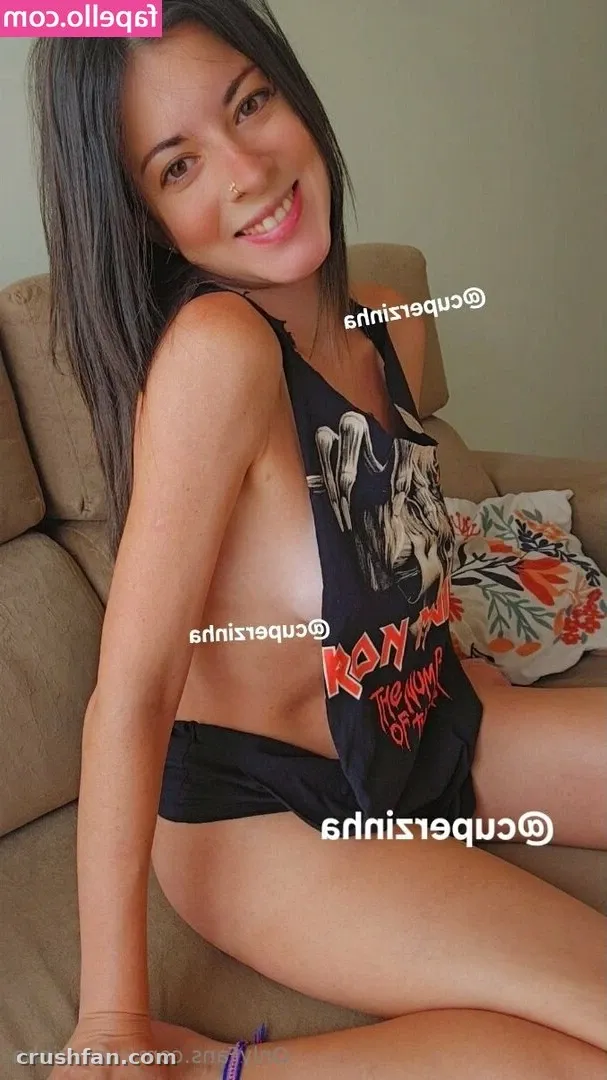 Cuperzinha sonriendo mientras está sentada en un sofá beige con un top gráfico oscuro