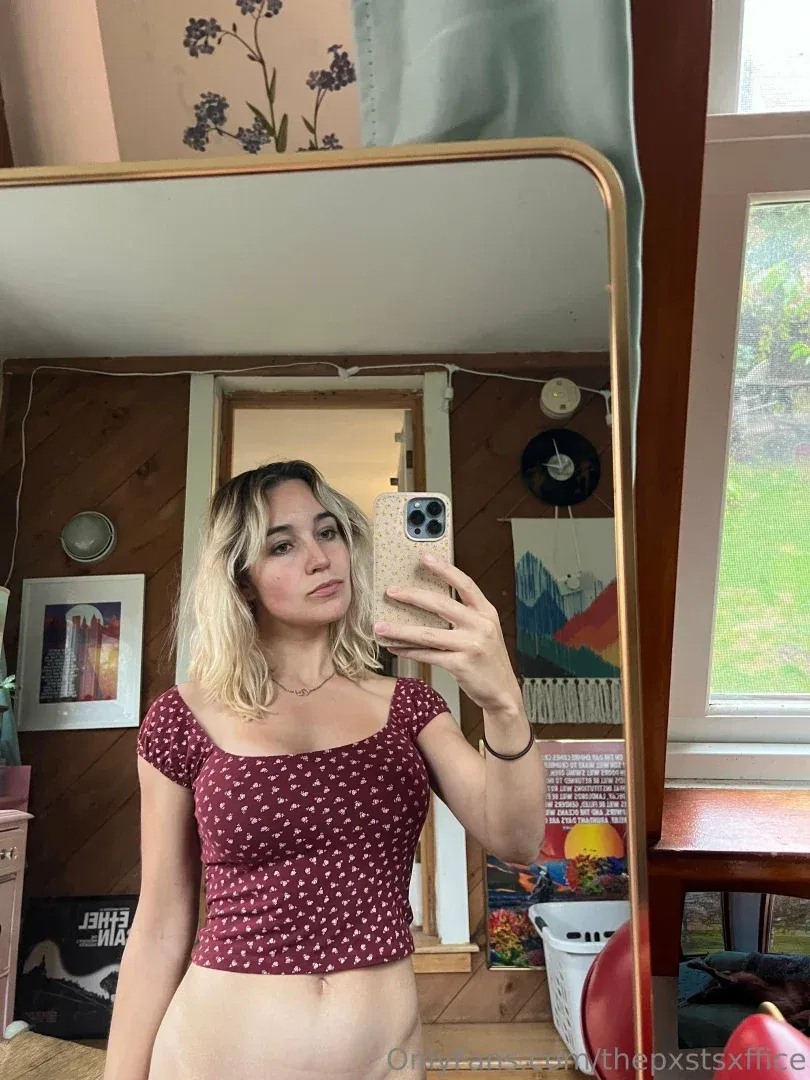 Maizie dans un haut rouge à motifs prenant un selfie dans le miroir dans une pièce lambrissée de bois.