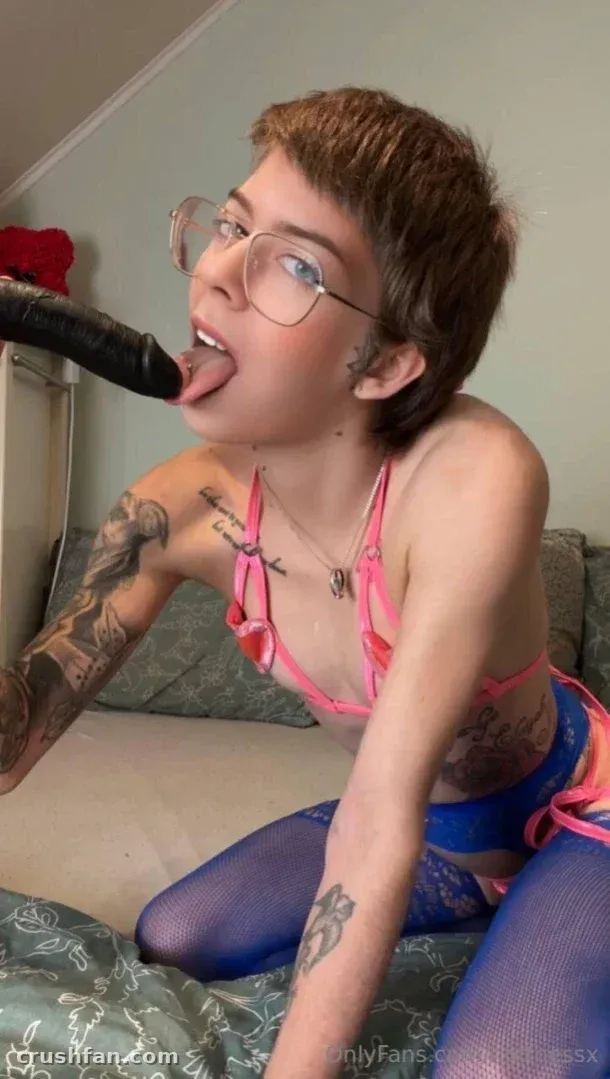 Creator in glasses, pink top and blue tights posing indoors on a couch