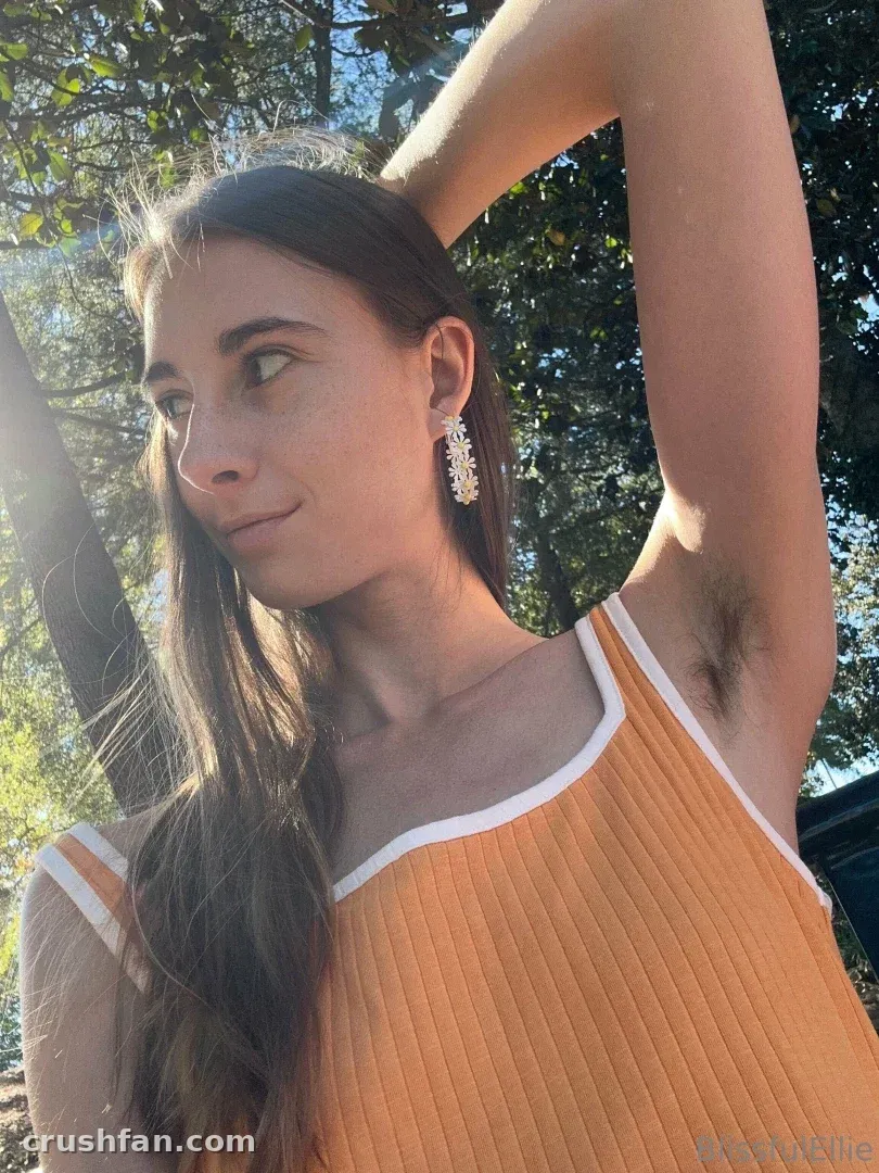 Ellie in an orange ribbed top outdoors with trees behind her