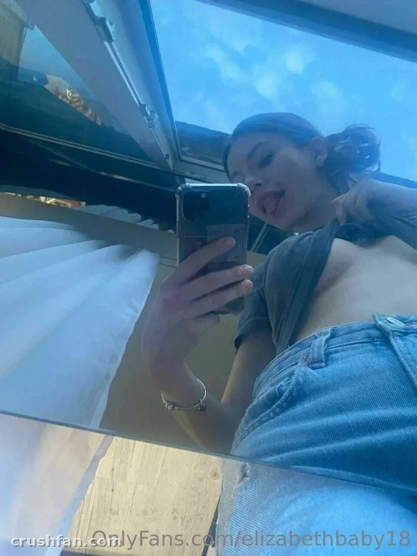 Elizabeth prenant un selfie miroir avec un haut gris et un jean bleu.