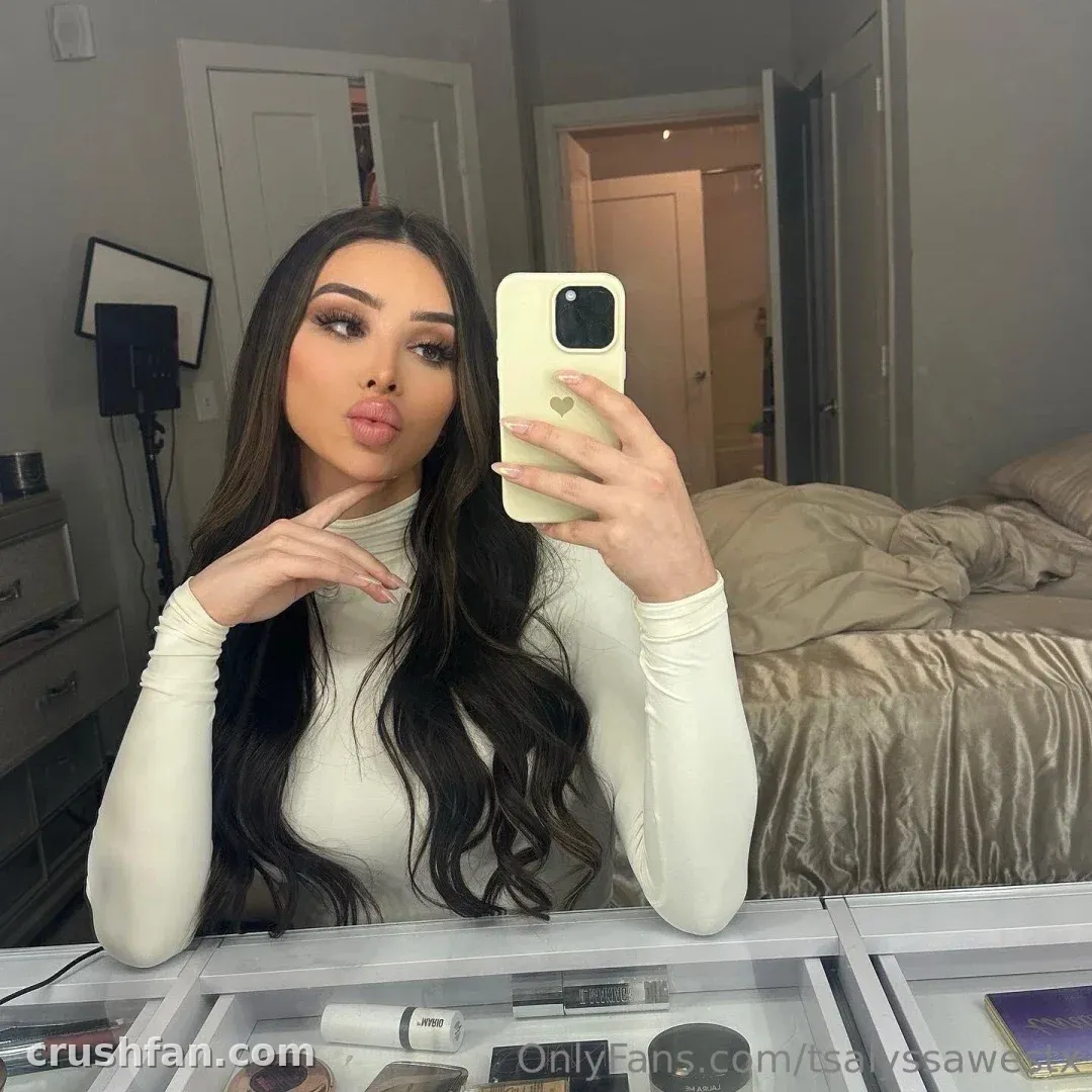 Alyssa in einem cremefarbenen Rollkragenpullover beim Spiegel-Selfie in einem Schlafzimmer mit beiger Bettwäsche