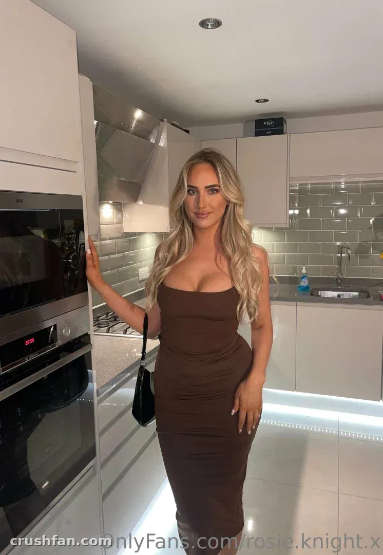 Rosie in a long brown dress standing in a modern white kitchen.