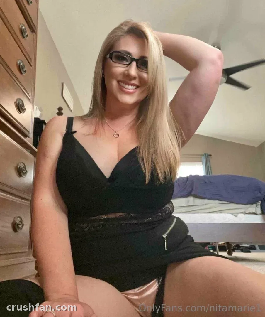 Nita Marie em um top preto com acabamento de renda sorrindo em um ambiente de quarto