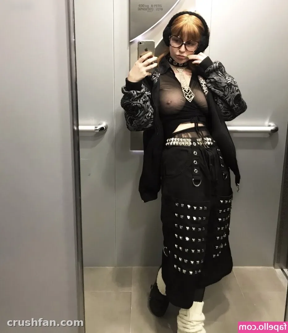 Creator in a black sheer top, studded skirt and jacket taking an elevator mirror selfie