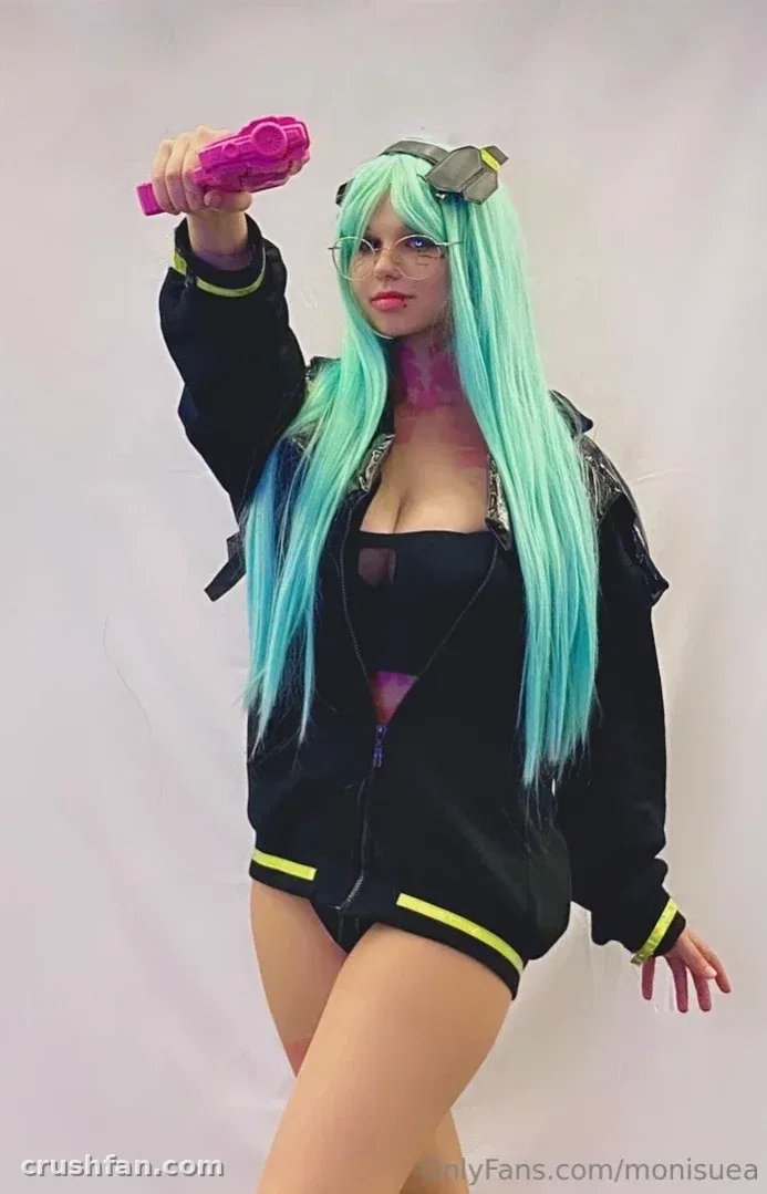 Monii♡ in a mint-green wig and black jacket holding a pink toy blaster against a white background.