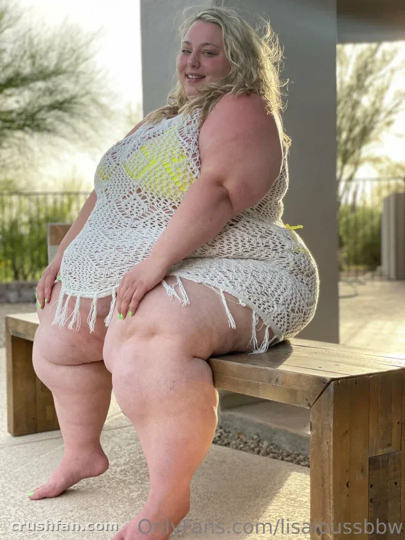 LisaLou sentada en un banco de madera al aire libre con un cubre-todo de crochet blanco sobre un top amarillo.