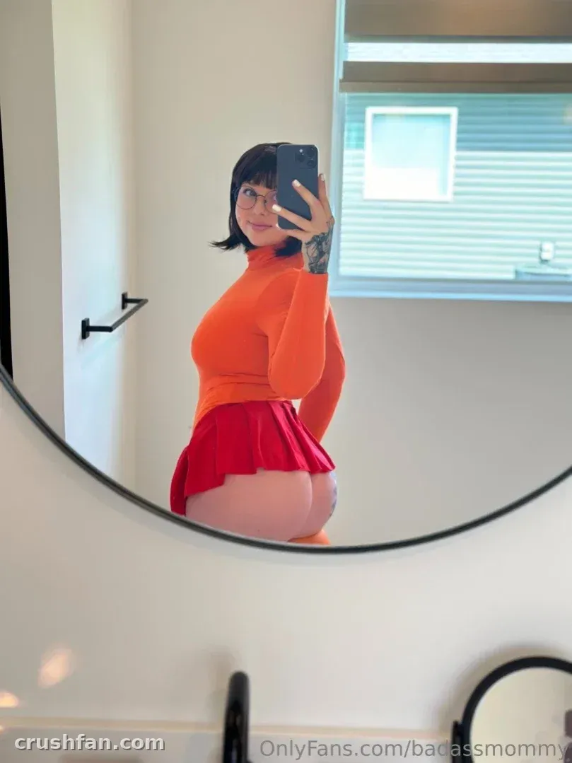 Sara in einem orangefarbenen Top und rotem Rock beim Spiegel-Selfie in Innenräumen