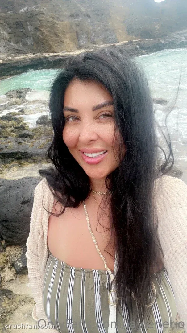 Femme souriante aux longs cheveux foncés, en haut rayé et gilet en maille sur un rivage rocheux