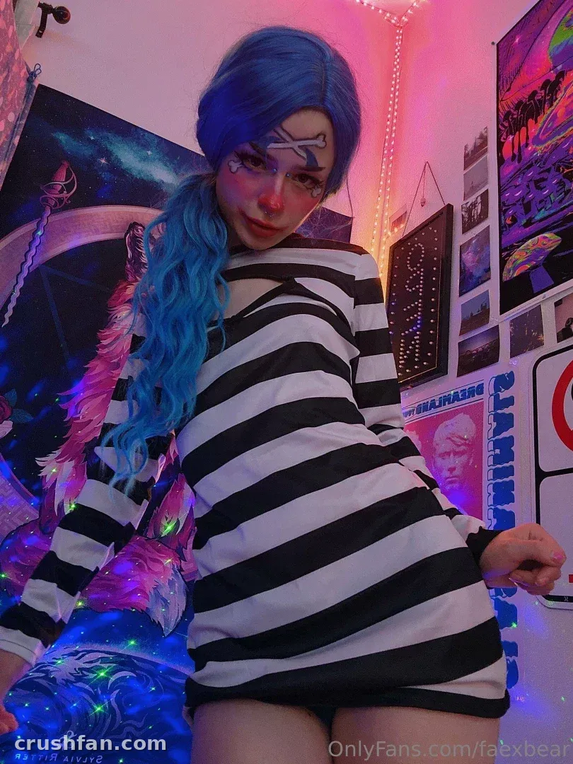 Fae with blue hair and a striped top posing in a neon-lit room with posters.