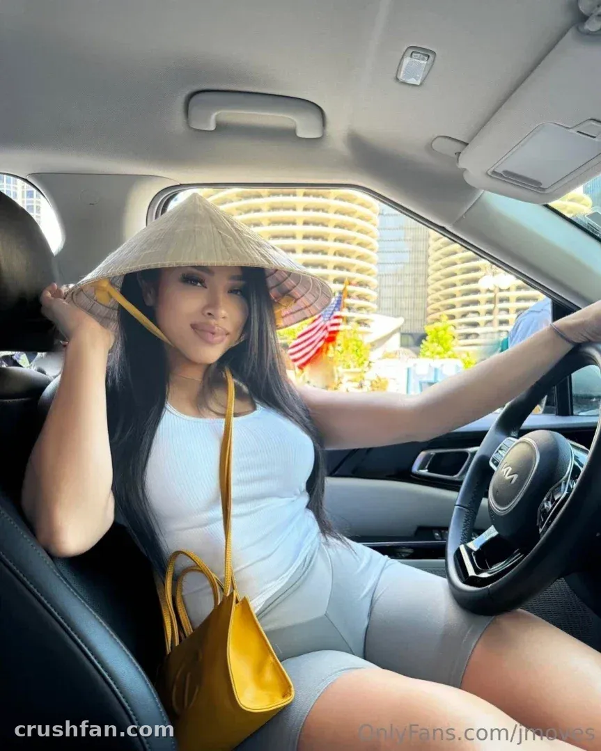 Jade dans une voiture tenant un chapeau conique, portant un haut blanc et un short gris.