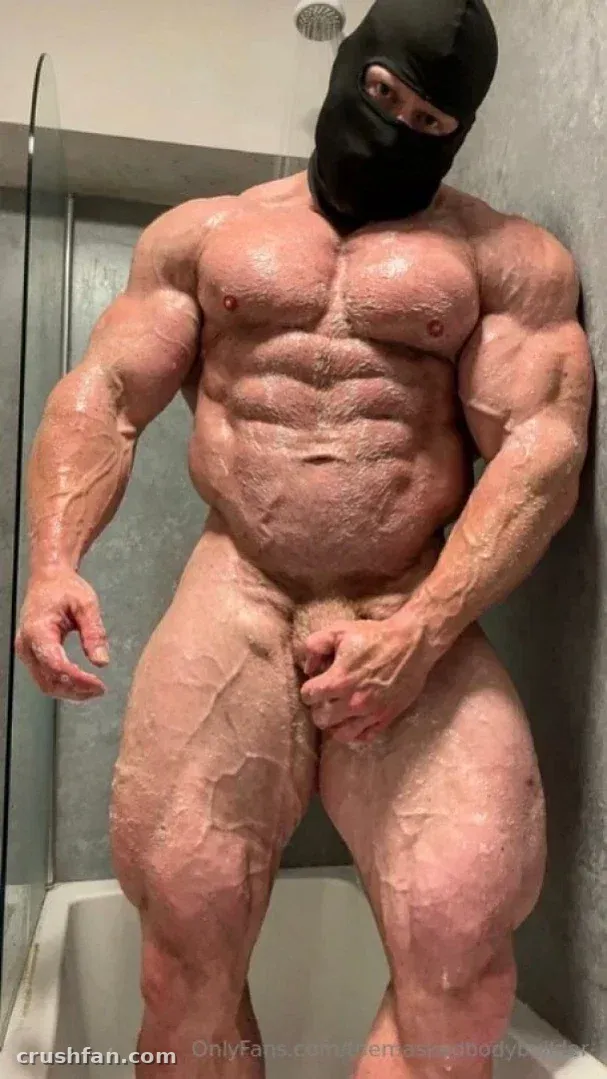 Muscular man in a black balaclava standing in a tiled shower, full-body view.