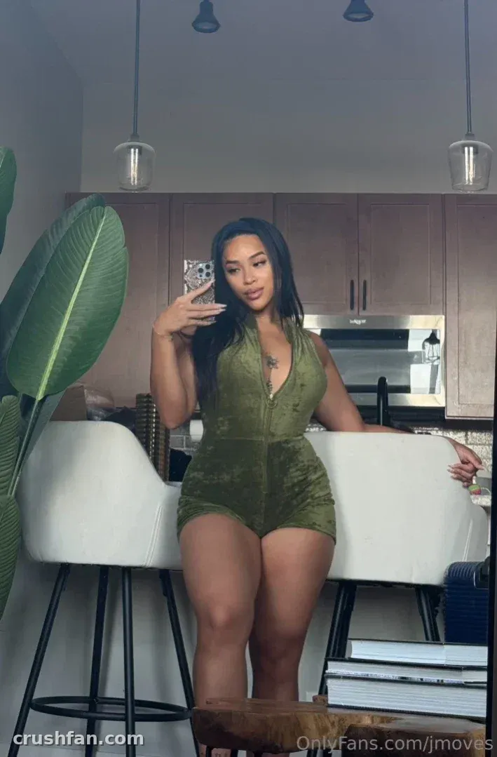 Jade dans une combinaison vert olive prenant un selfie dans le miroir dans une cuisine moderne.