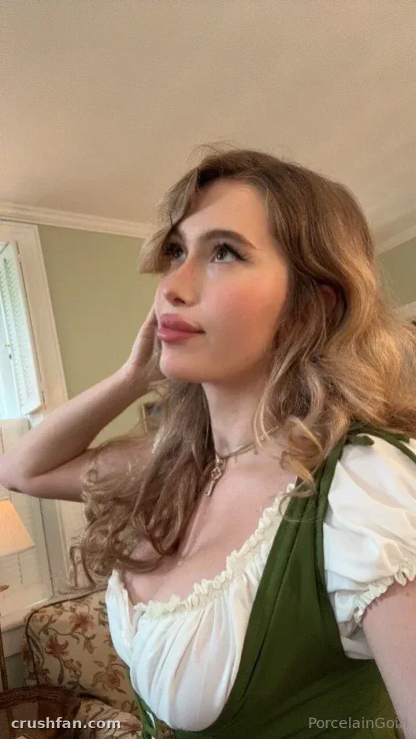 Rosealine in a green dress and white top indoors, looking upward in warm light