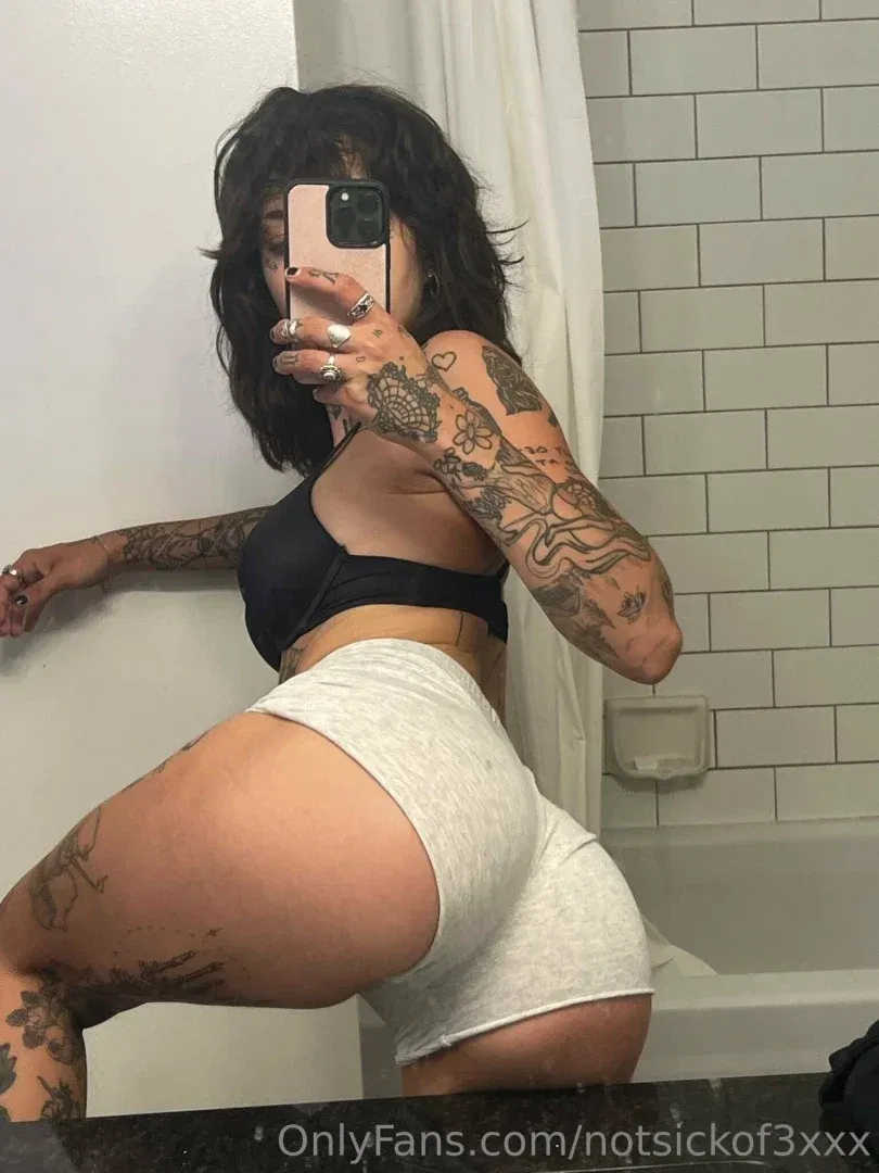 Keaton Belle taking a mirror selfie in a bathroom wearing a black top and light shorts.