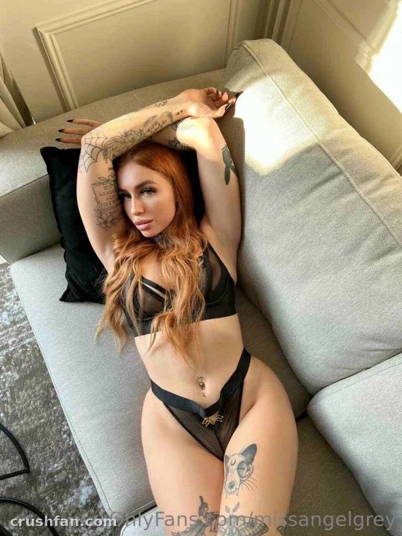 Missangelgrey en lingerie en résille noire allongée sur un canapé gris avec des tatouages visibles