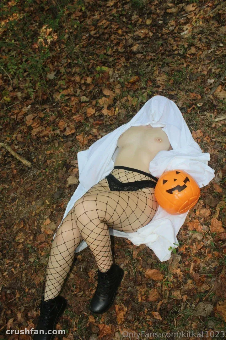 Katie R. lying on autumn leaves with a pumpkin and white fabric outdoors.