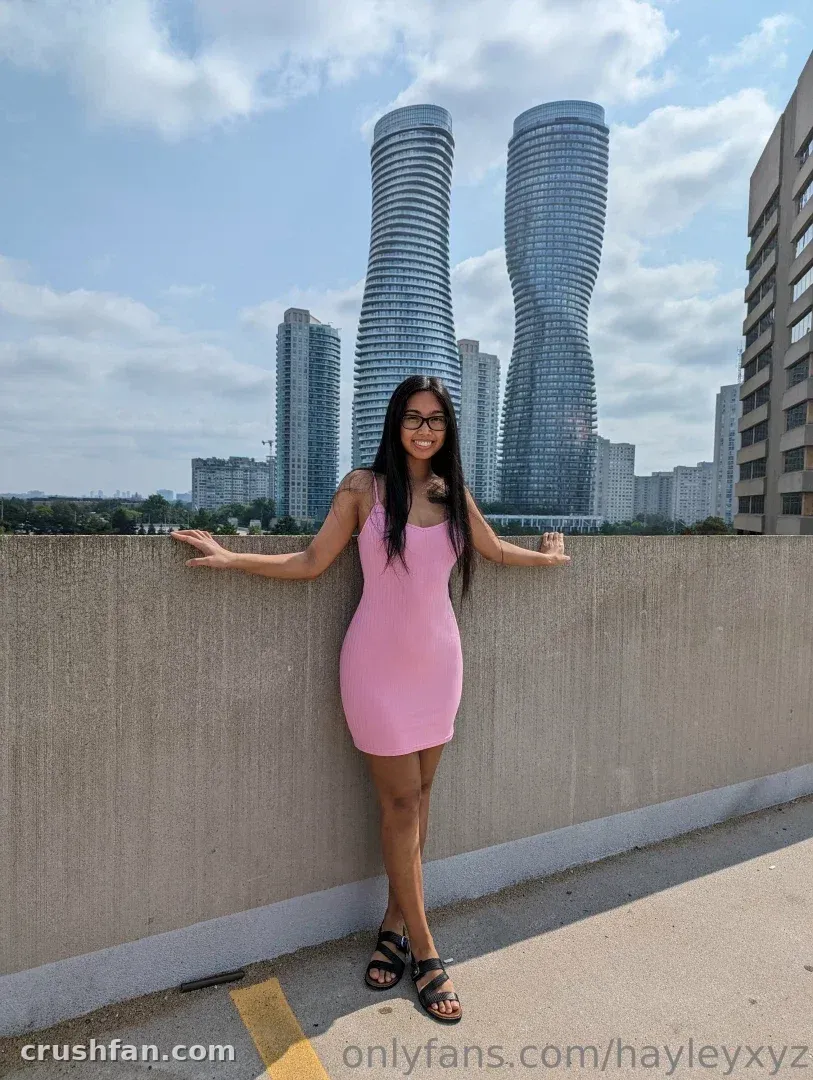 Creator in a pink dress standing on a concrete walkway with curved towers behind her.