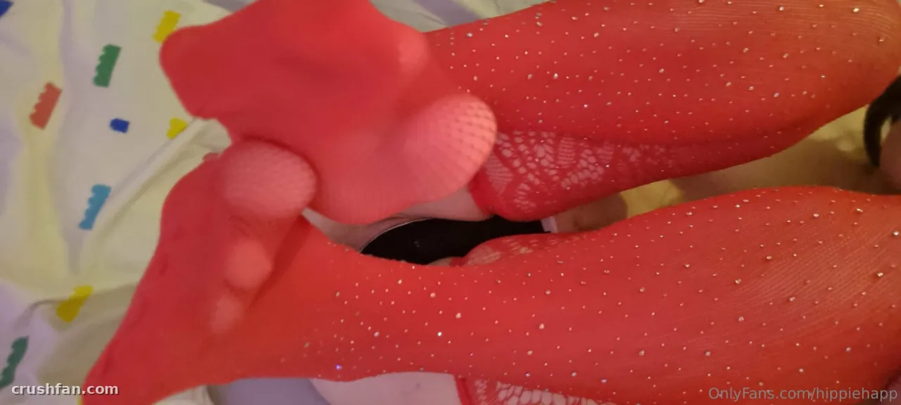 Close de pernas com meia-calça brilhante vermelha sobre um lençol branco com estampas coloridas