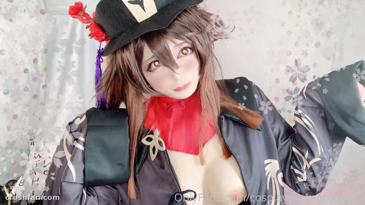 Cosplayer em um quimono floral escuro com peça de pescoço vermelha e um chapéu decorado, posando em ambiente interno