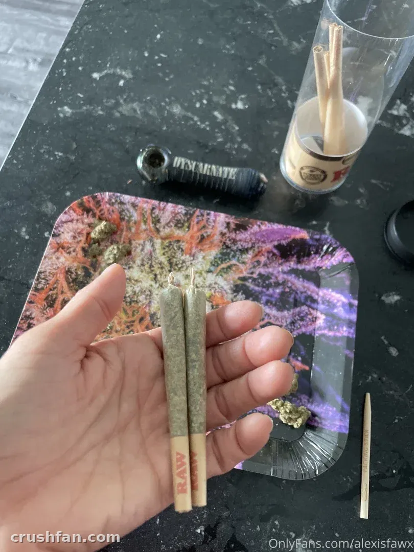 Alexis Fawx holding two rolled joints above a purple cosmic rolling tray on a dark counter.