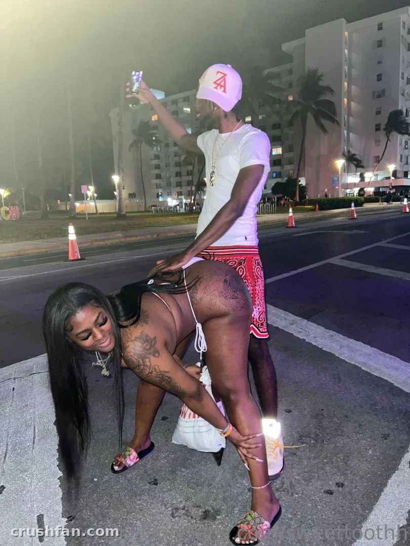 Sweettoothh on a night street in a bikini with a person standing behind her