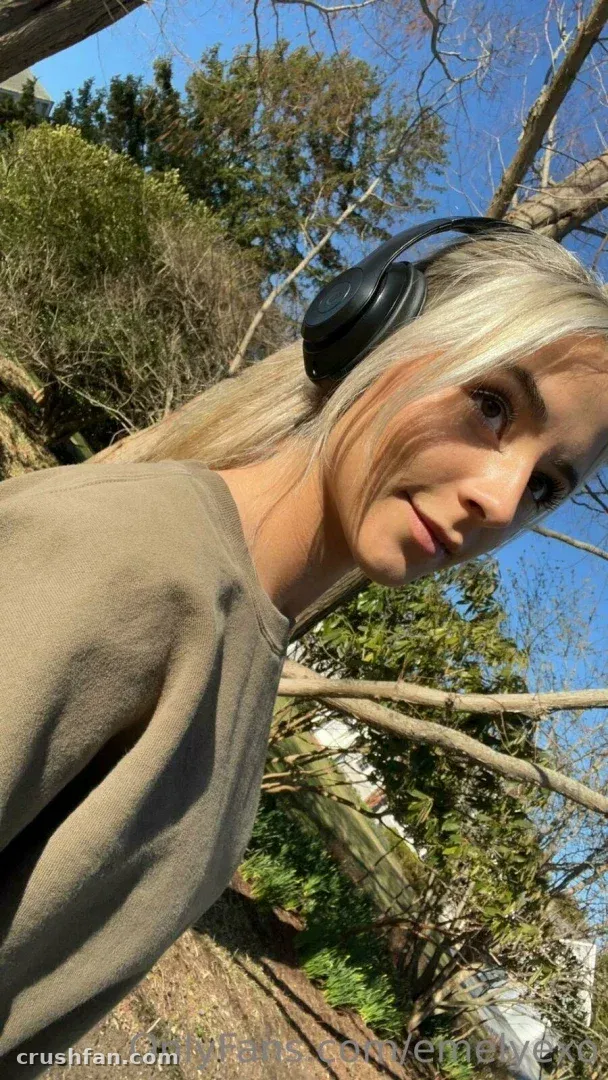 Em in a beige top and black headphones outdoors under a blue sky.
